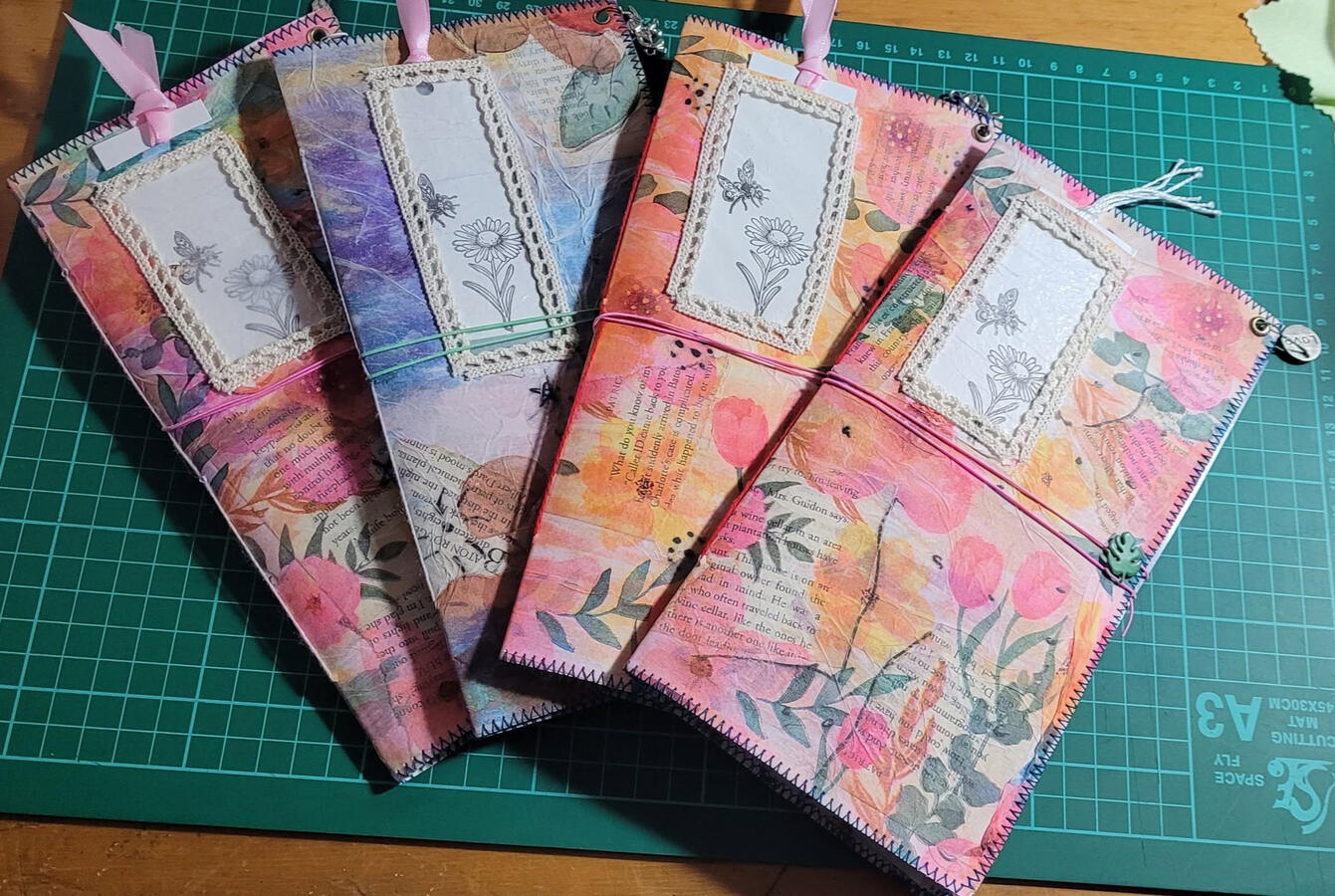 Final stage. These journals have had their cover dangles added, their elastic closures secured, and their cute little flower tags added to peek through the window part of the original envelope. Final stage. These journals have had their cover dangles added, their elastic closures secured, and their cute little flower tags added to peek through the window part of the original envelope.